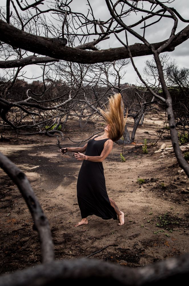 Woman posing on ground near dry trees