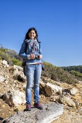 Smiling female dressed in blue standing on coastal rocks taking picture