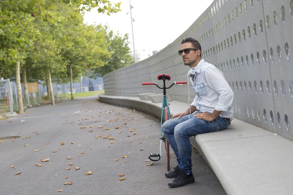 Male in sunglasses sitting on long outdoor seating near park
