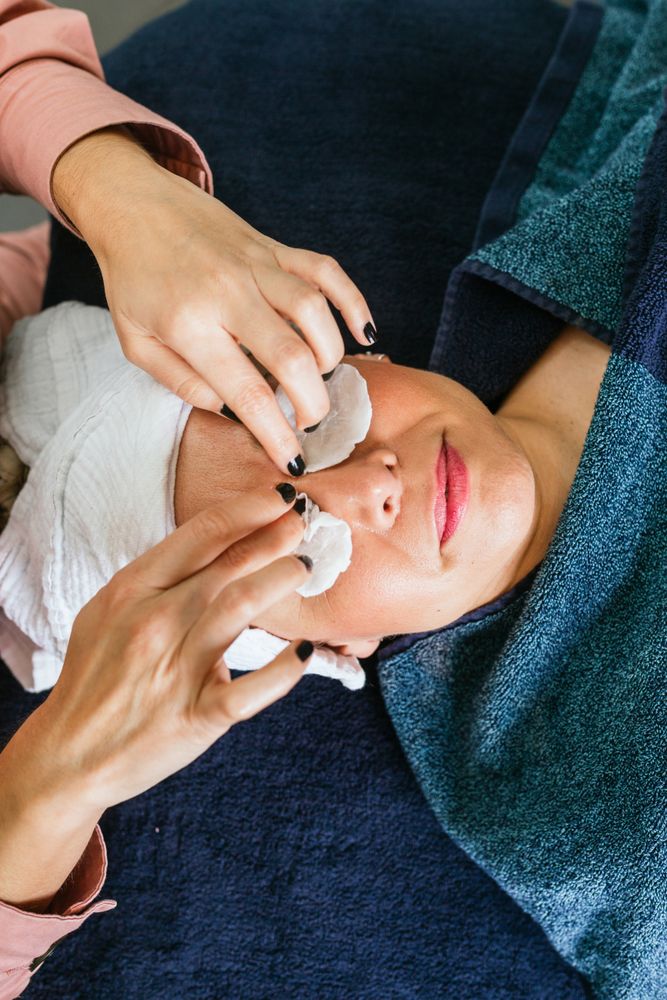 Crop beautician applying toner on face of female client in beauty salon