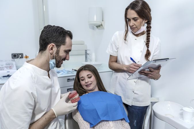 Young woman is sitting in dental chair in clinic with dentist is showing model of jaw
