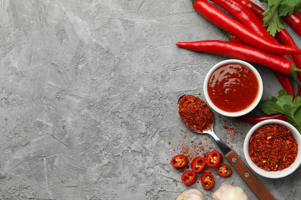Composition with chilli pepper, powder spice, garlic and sauce on gray background