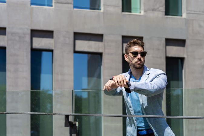 Portrait of a young bearded man with sunglasses standing outdoors in the city while looking aside