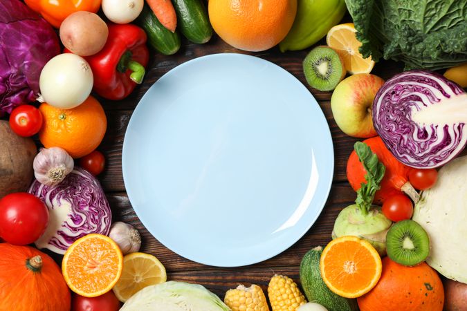 Different vegetables and fruits, and plate on wooden background, top view