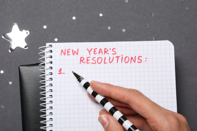 Pen in hand and notepad with text on gray background, close up