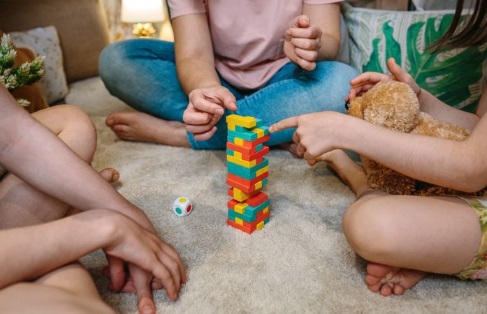 Unrecognizable family having fun playing with wooden stacking piece game over carpet at home