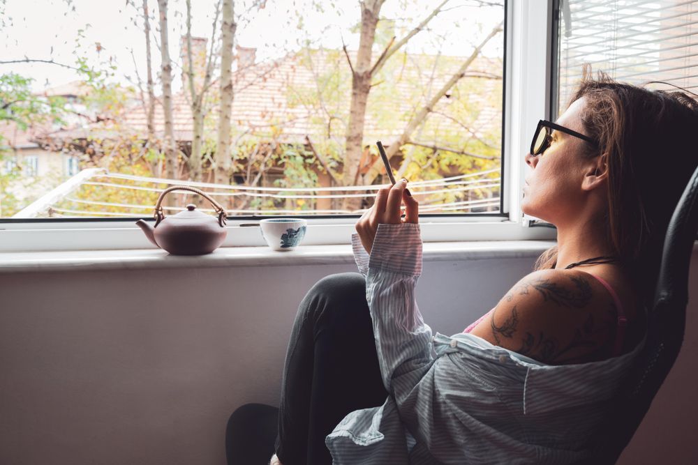 Woman relaxing with tea pot and spliff by the window