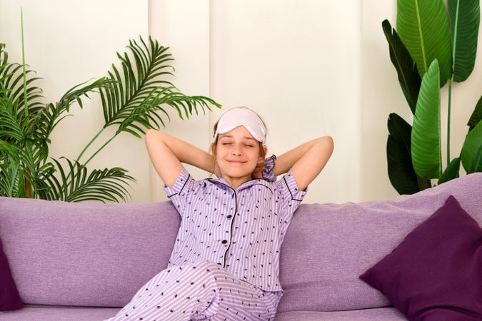 Relaxed girl in pajamas with sleep mask on couch.