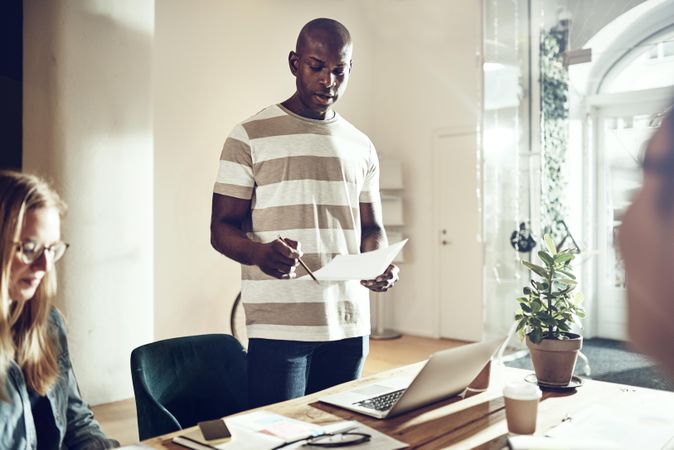 Man standing at table reading off a paper in hand to colleagues