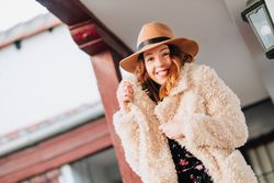 Smiling woman in warm wear standing near building and fence