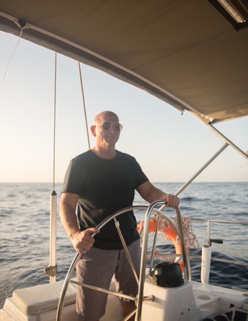 Smiling man holding steering wheel on yacht on water near quay