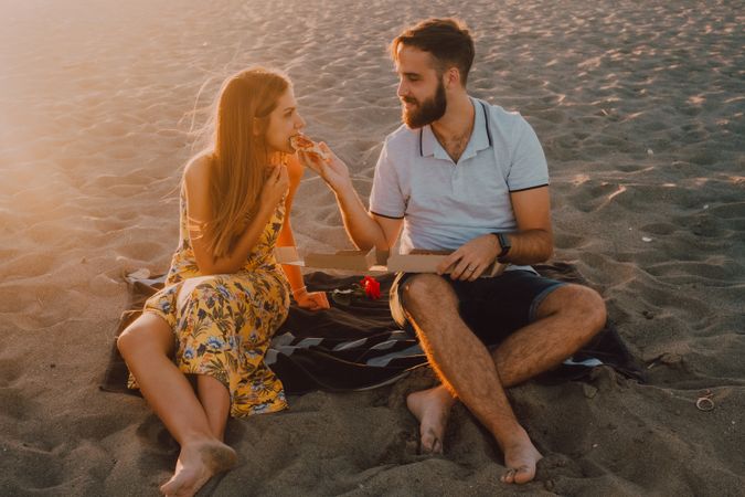 Lovely couple eating pizza together at sandy beach