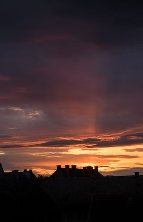 Sun setting in dark sky with silhouette of roof
