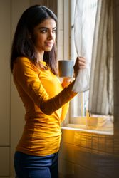 Vertical composition of woman gazing out the window with warm beverage