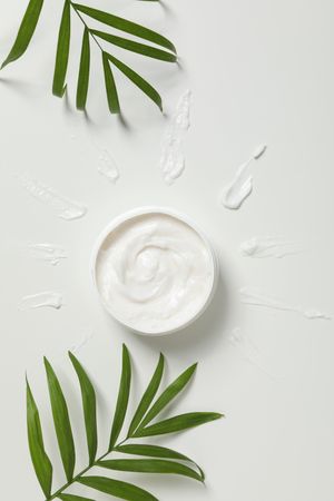 Jar with cream and leaves on light background, top view