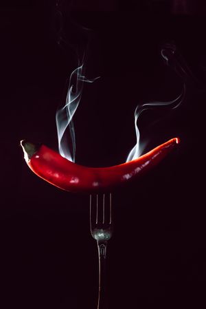 red chili pepper on fire in fork on a dark background