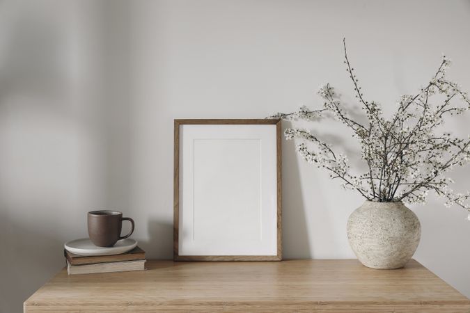 Vertical wooden picture frame, poster mockup in sunlight on desk