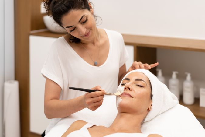 Woman with towel on head having a relaxing face mask applied at beauty spa