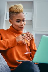 Black woman with a champagne flute while watching something on her laptop