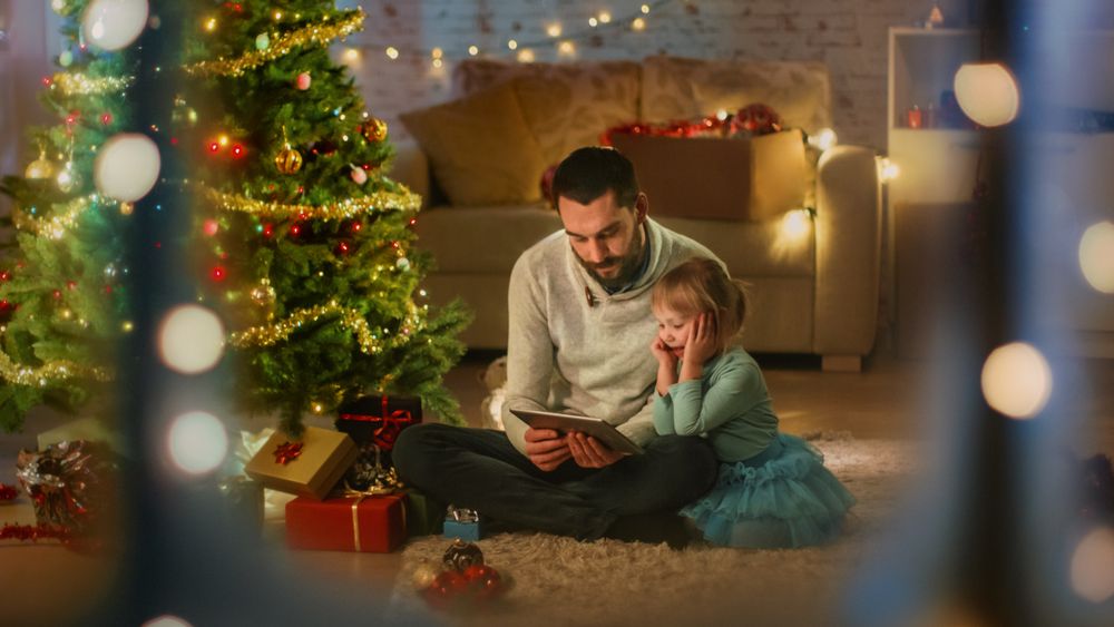 Father Reads Book to His Daughter, Sitting Under Christmas Three with Gifts.