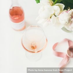 Glass of pink rose wine, and bottle with flowers and ribbon, square crop 0VE13b