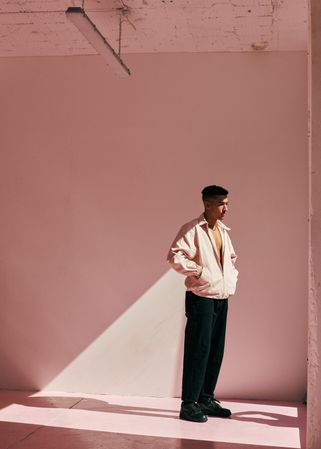 Young man posing in light pink room with a similar colored open jacket