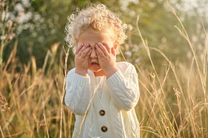 Funny little girl covering eyes with hands in nature