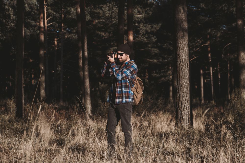 Confident photographer taking picture with camera in sunny forest