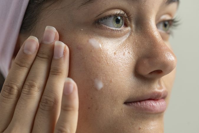 Macro of a woman's face showing skin texture while applying a luxury moisturizing cream