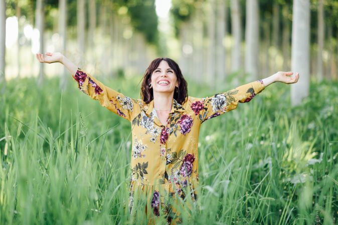 Smiling brunette female looking up in field of tall grass with open arms