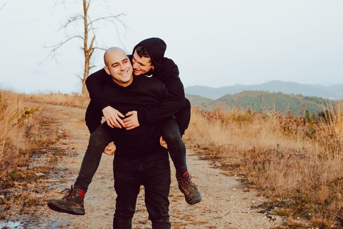 Smiling man holding on back cheerful guy on road on hill