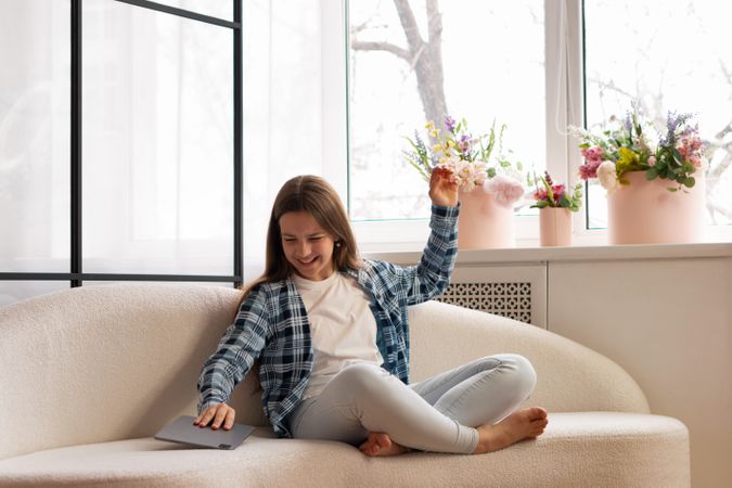 Smiling teen girl playfully placing tablet aside on sofa.