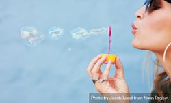 Close up side view shot of young female model blowing soap bubbles on blue background 5RYaN0