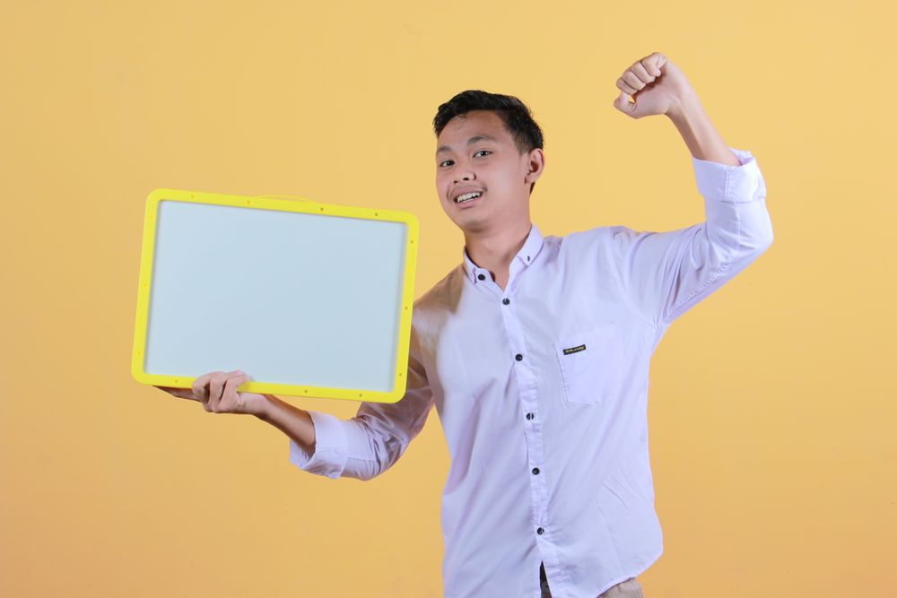 Portrait of a young man in yellow backdrop holding a blank note board