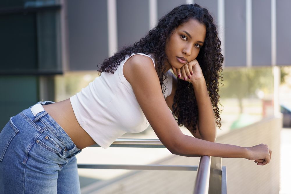 A Stylish Young Woman is Posing Outdoors with her Curly Hair in the Bright Sunlight