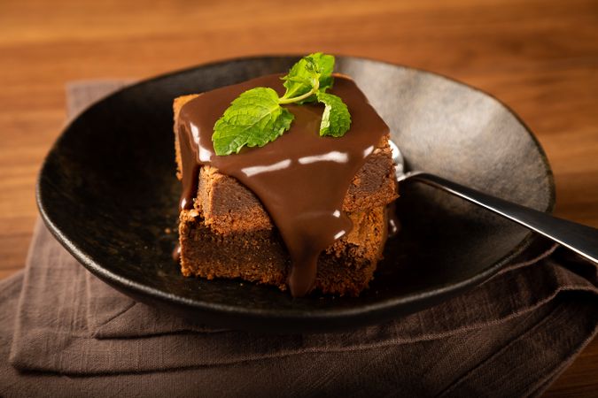 Chocolate brownies with syrup and fresh mint leaves served on dark plate