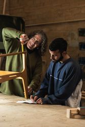 Craftsman creating wooden chair with coworker drawing sketches