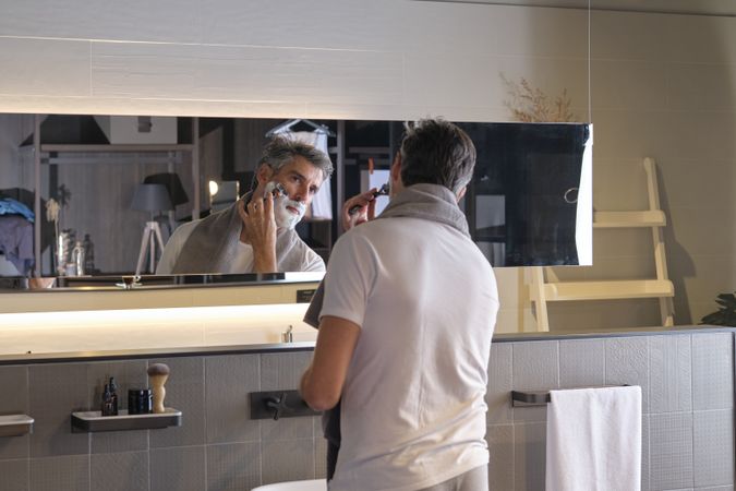 Adult male looking at mirror and shaving using razor