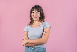 Happy woman wearing a pink breast cancer awareness ribbon while looking at camera