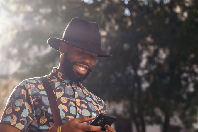 Stylish Black man walking on the city street using smartphone