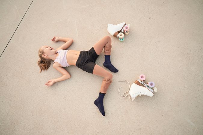 Laughing girl lying on concrete ground near quad roller skates