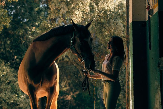 Horsewoman standing with horse in barn