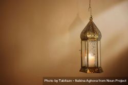 Hanginng decorative brass Moroccan lantern glowing at night. Blurred golden background with light beams. Ramadan Kareem, Eid ul Fitr muslim holiday still life. Festive celebration concept, banner. 0yXamW