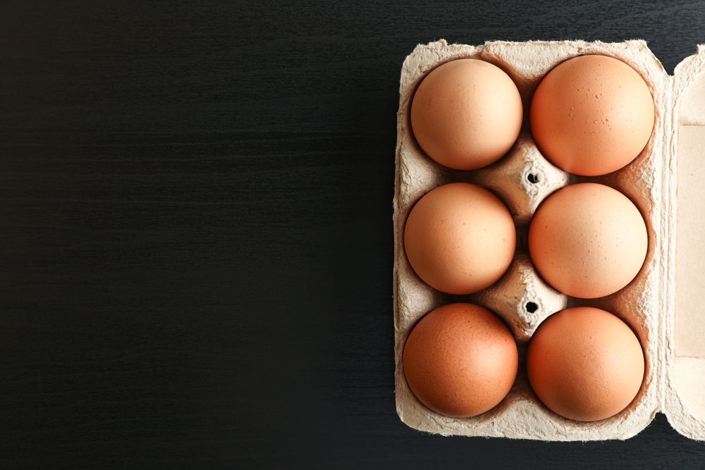 Brown chicken eggs in carton box on dark background, space for text and top view
