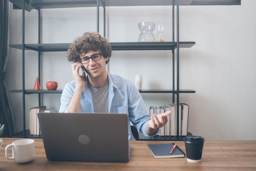 Creative designer sitting at his desk talking on the phone with customer