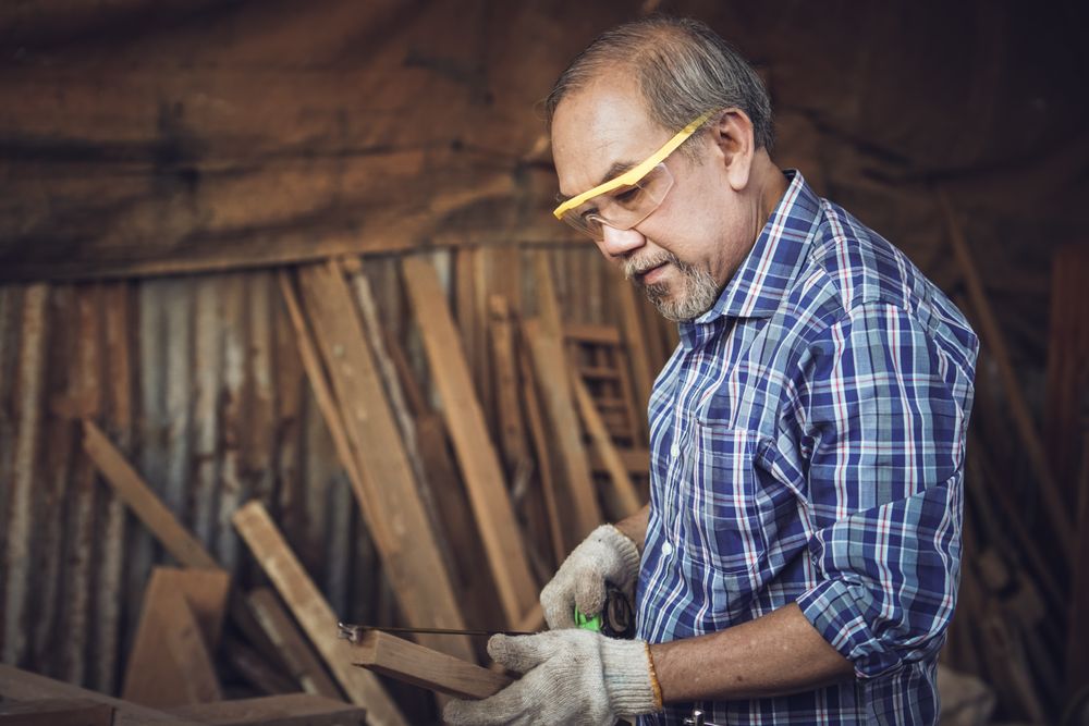 Asian male carpenter with measuring tape over a wooden plank in the carpentry workshop