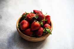 Strawberries in wooden bowl full on grey counter with copy space