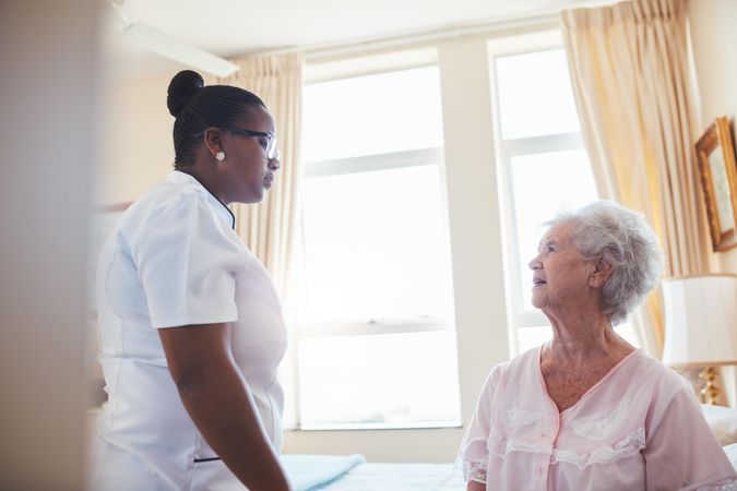 Nurse talking with mature woman sitting on bed