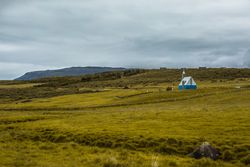 Small house in green filed under cloudy sky