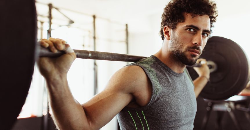Confident young man exercising with barbell at fitness center
